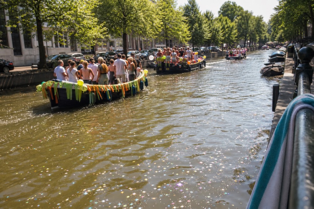 Decorated boats moving along an Amsterdam canal during a summer parade, no text, no logos, no people.