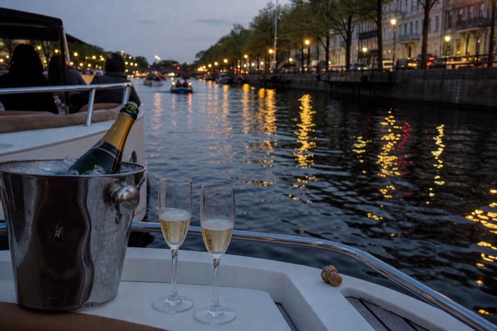 A champagne bottle and glasses on the deck of a private canal boat at dusk, no text, no logos, no people.