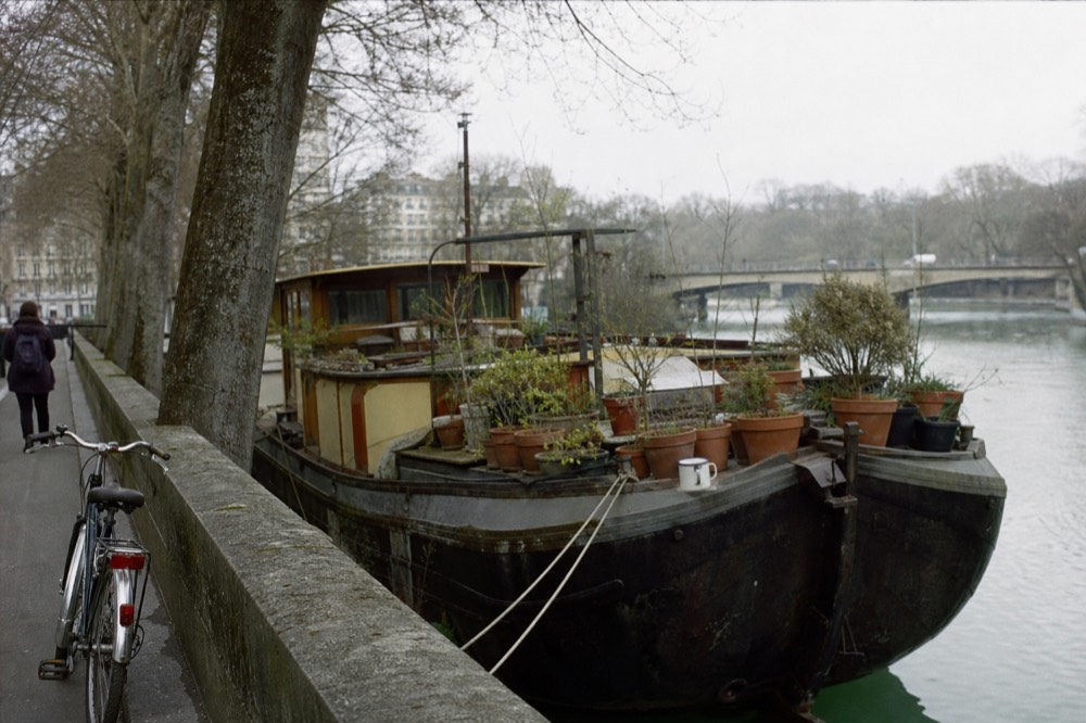 A classic Dutch barge houseboat with potted plants on its deck moored on an Amsterdam canal, no text, no logos, no people