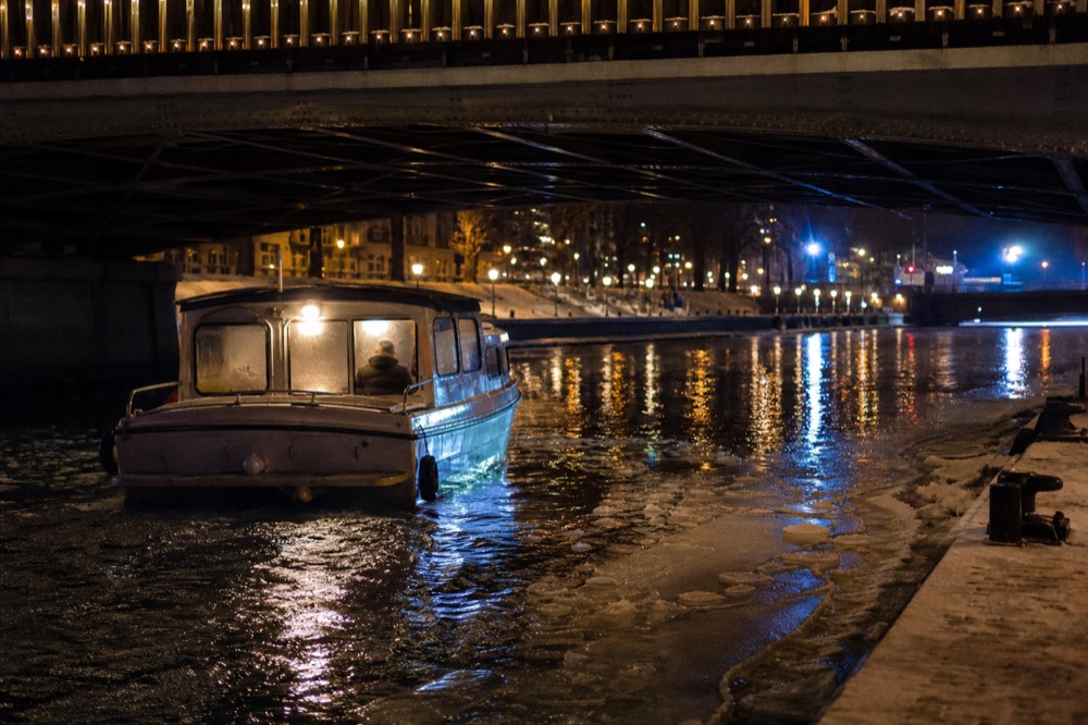 A canal boat passing under a lit Amsterdam bridge at night, no text, no logos, no people