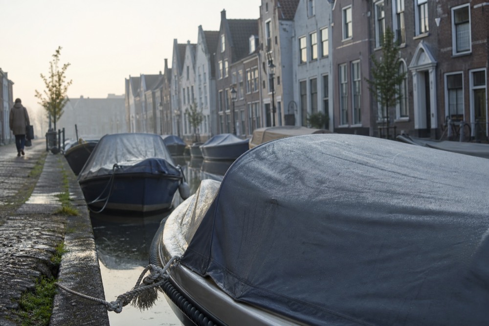 Canal boats moored along a narrow Amsterdam canal with classic gabled facades, no text, no logos, no people