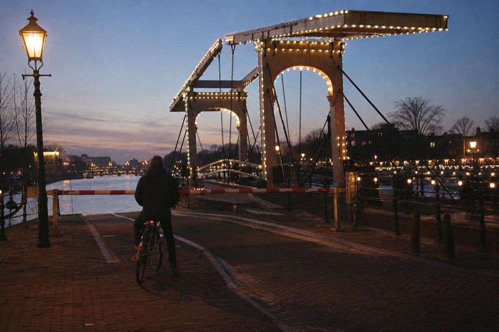 A classic Dutch drawbridge over an Amsterdam canal at dusk with warm streetlights, no text, no logos, no people