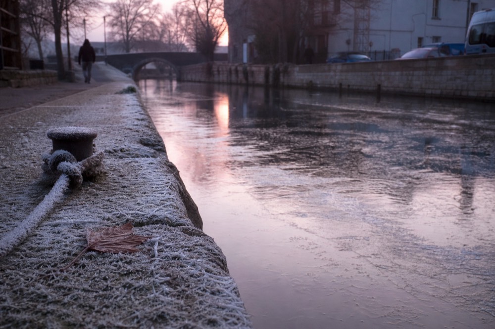 Ice crystals forming at the edge of an Amsterdam canal in early morning light, no text, no logos, no people