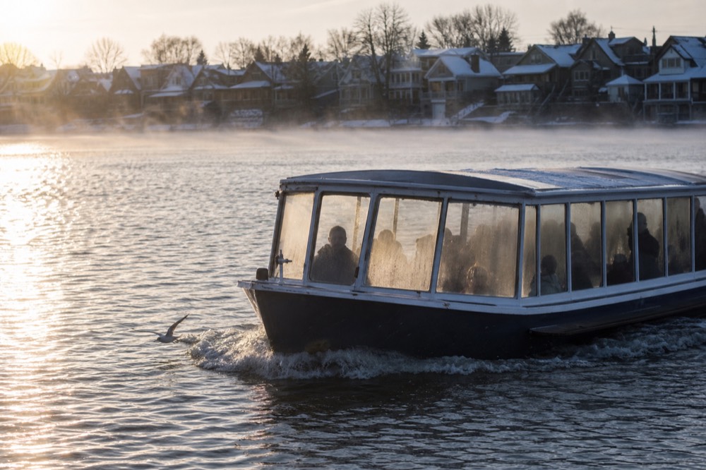 A covered canal cruise boat gliding past frosted gabled houses on open winter water, no text, no logos, no people