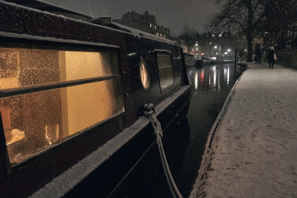 Warm light glowing from the windows of a covered canal boat moored along a quiet winter canal, no text, no logos, no people
