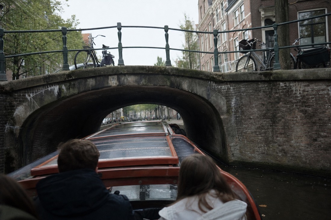 A covered saloon boat passing under a canal bridge near the Jordaan district, no text, no logos, no people.
