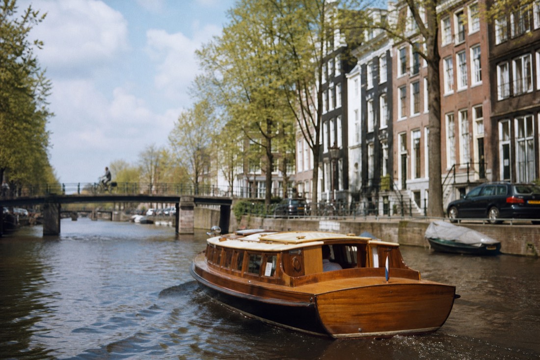 A classic saloon boat gliding along an Amsterdam canal lined with gabled houses, no text, no logos, no people
