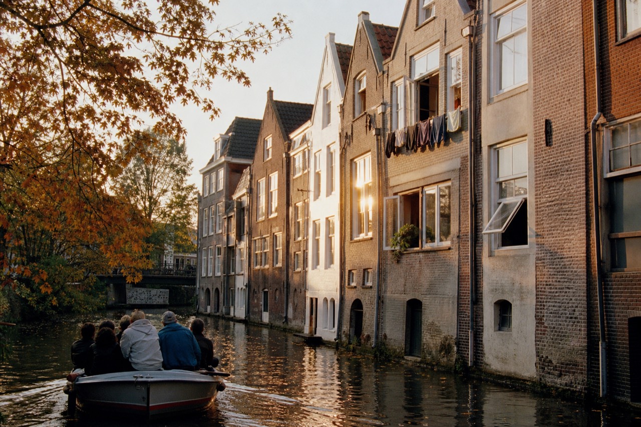 A canal boat passing gabled merchant houses along an Amsterdam gracht at golden hour, no text, no logos, no people