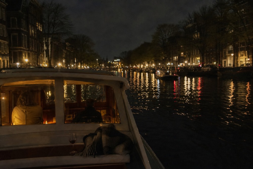 An evening canal boat lit by city lights reflected in dark canal water, no text, no logos, no people