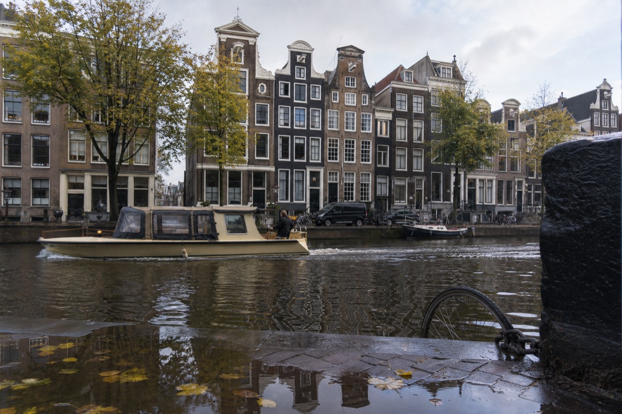 A canal boat passing gabled houses on an Amsterdam gracht, no text, no logos, no people