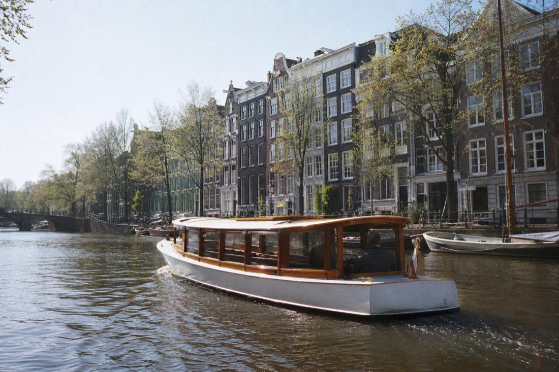 A classic saloon boat gliding along the Herengracht past gabled merchant houses, no text, no logos, no people.