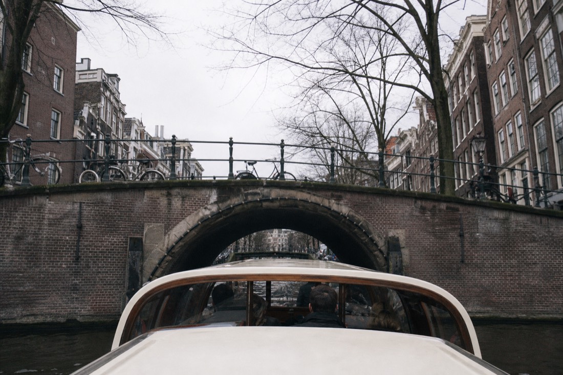 A low canal cruise boat passing under one of Amsterdam's arched stone bridges, no text, no logos, no people