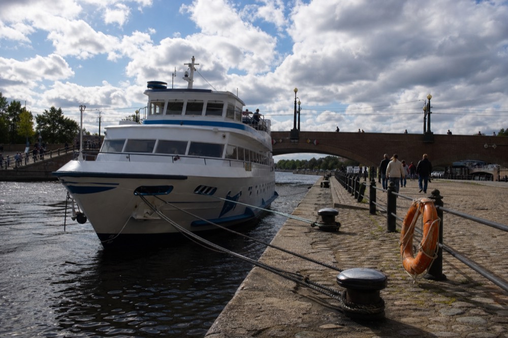 A moored canal cruise boat at a stone quay beside a brick bridge in central Amsterdam, no text, no logos, no people