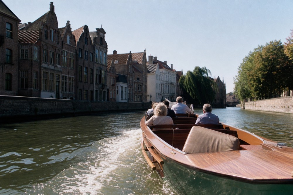 A classic Amsterdam saloon boat with wooden benches cruising past merchant houses, no text, no logos, no people