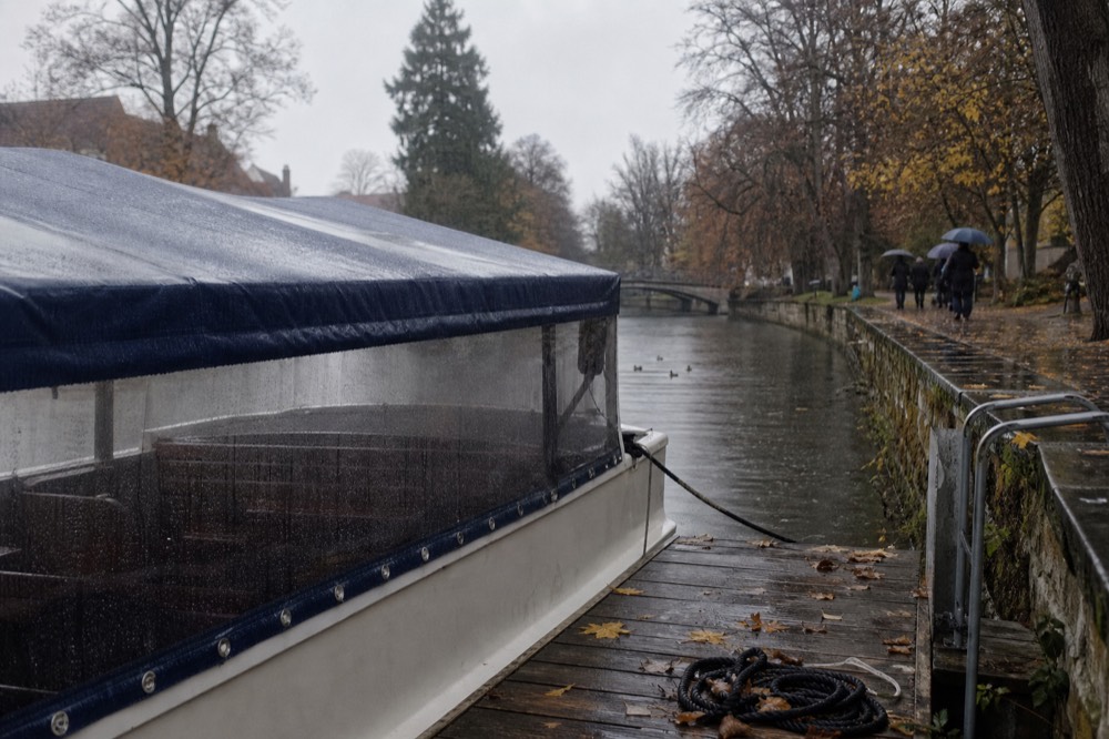A covered canal cruise boat moored at an Amsterdam jetty in soft rain, no text, no logos, no people