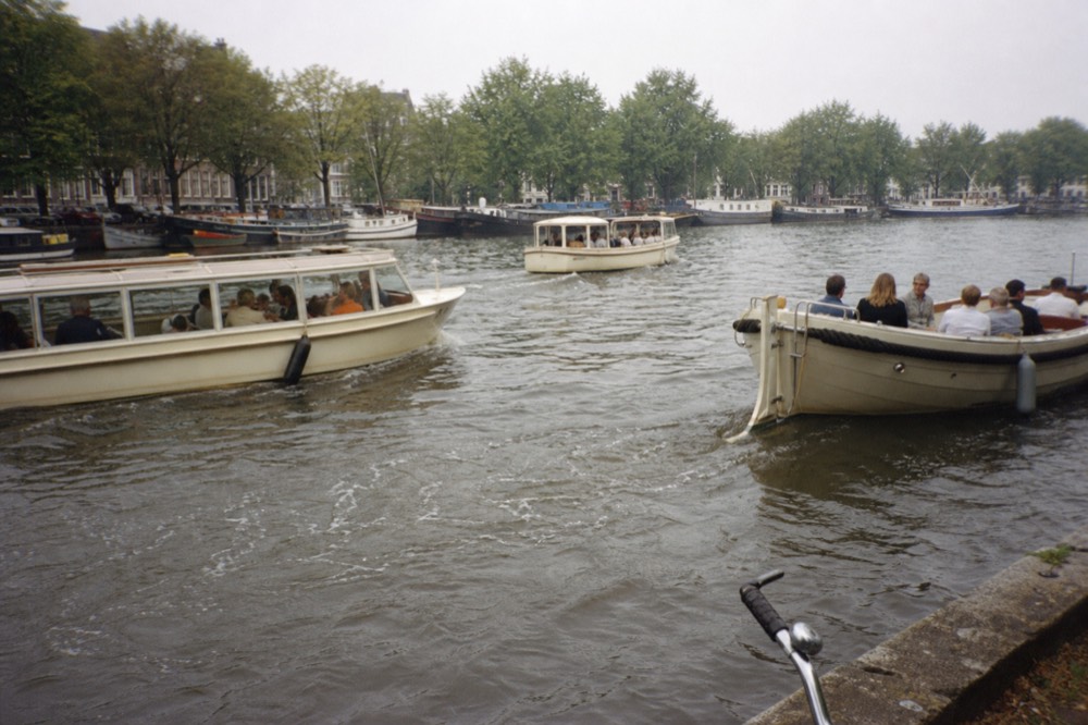 Several canal cruise boats passing each other on a busy Amsterdam gracht, no text, no logos, no people