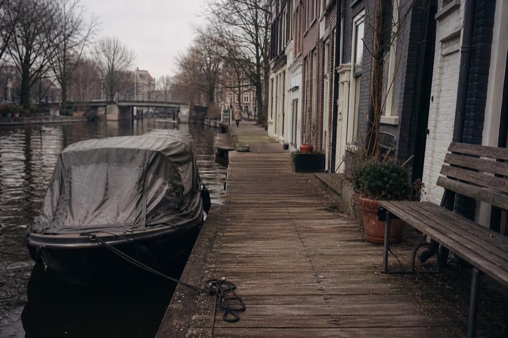 A covered canal cruise boat moored at a wooden jetty beside a row of Amsterdam canal houses, no text, no logos, no people