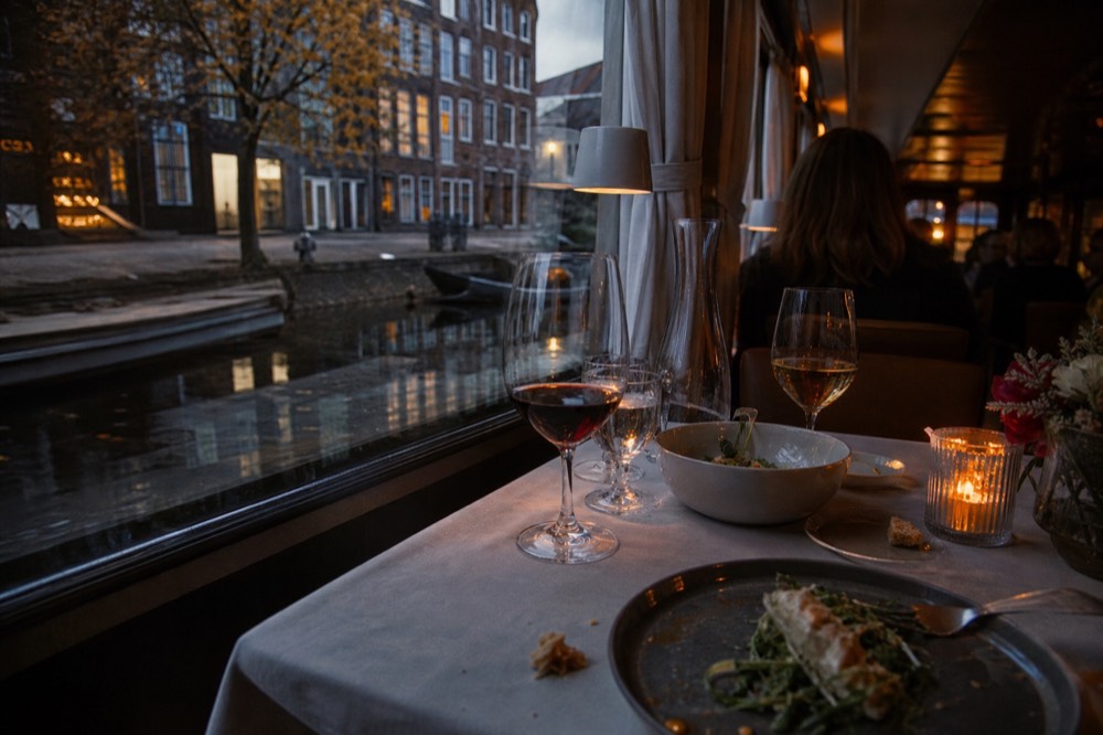 A candlelit dinner table set on a canal boat with wine glasses and plated food, no text, no logos, no people