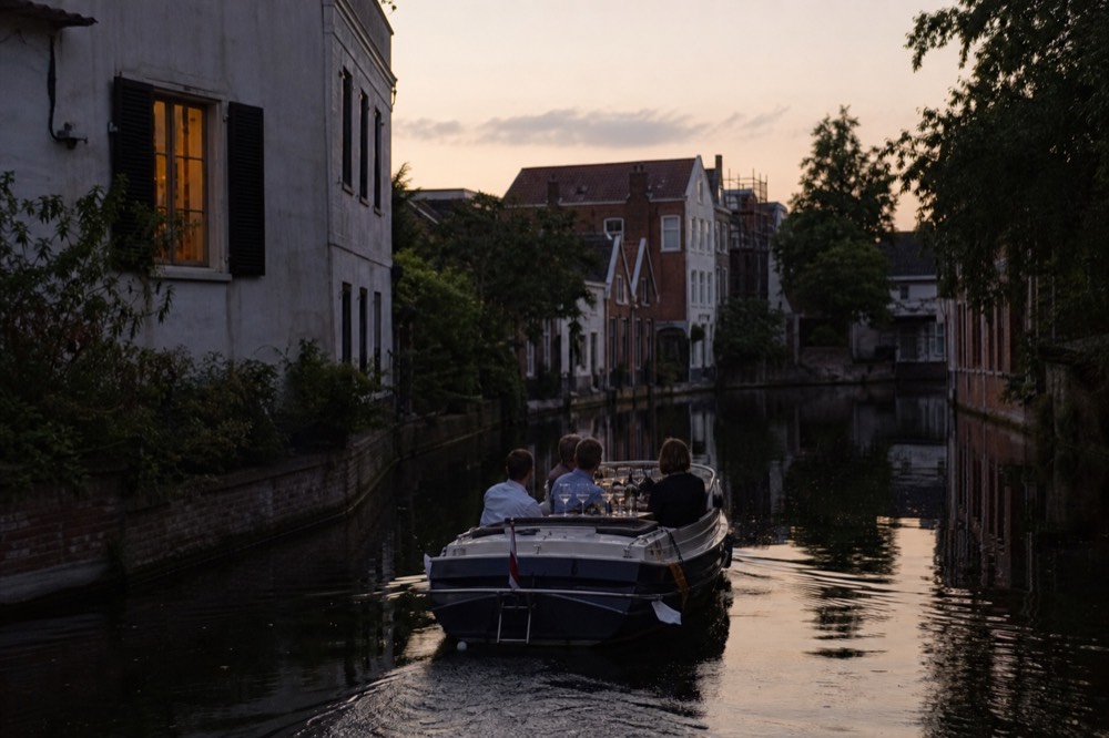 A small private saloon boat cruising an empty Amsterdam canal at dusk with champagne glasses on board, no text, no logos, no people