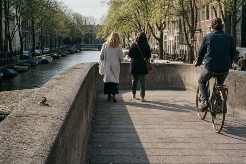 A cyclist and pedestrians crossing a classic Amsterdam bridge over a canal with boats moored below, no text, no logos, no people
