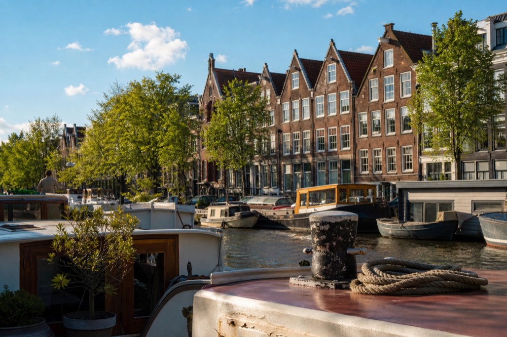 Sunlit Amsterdam canal with gabled houses and moored houseboats, no text, no logos, no people