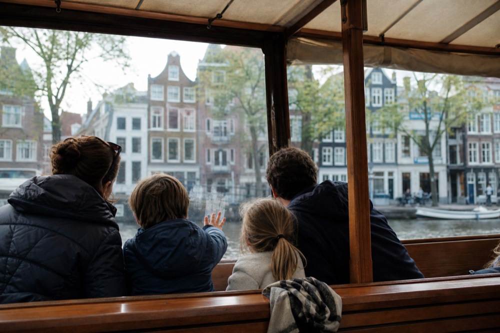 Family looking out from a covered canal cruise boat in daytime Amsterdam, no text, no logos, no people