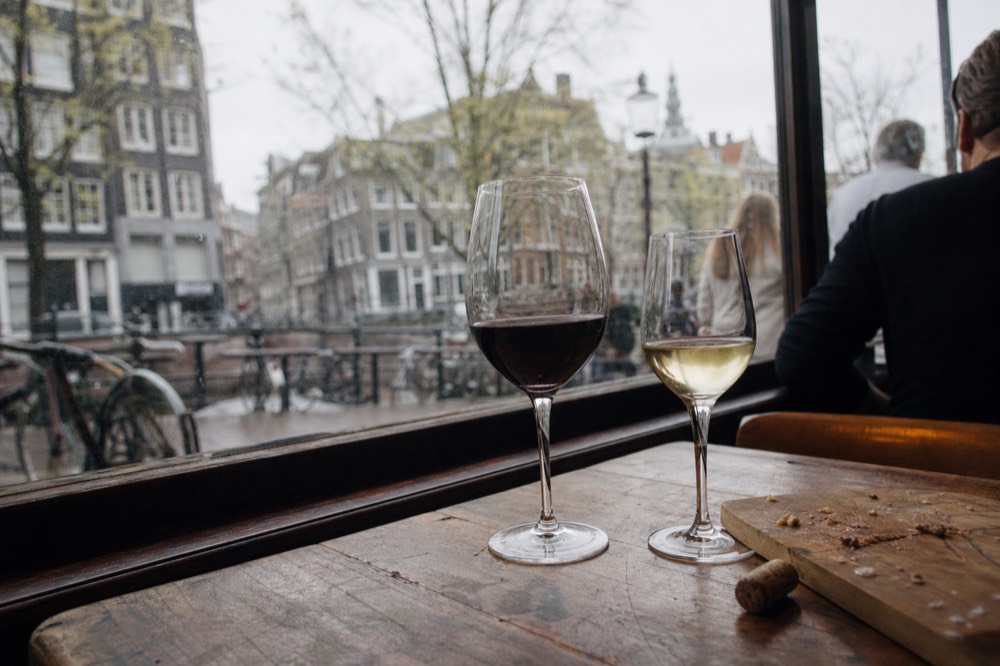 Wine glasses on a wooden saloon boat table with canal houses through the window, no text, no logos, no people.