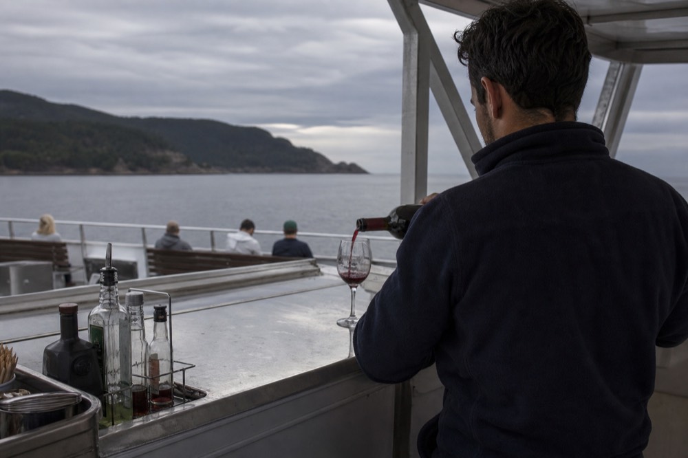 A crew member pouring wine behind a small boat bar, no text, no logos, no people.