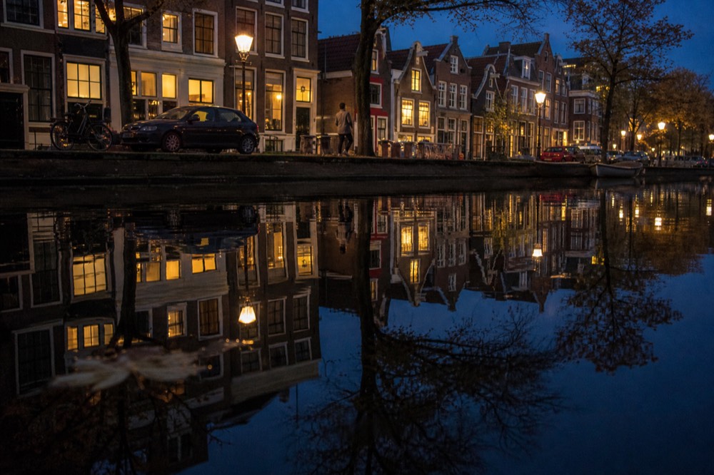 Canal houses reflected in dark water with evening lights, no text, no logos, no people.