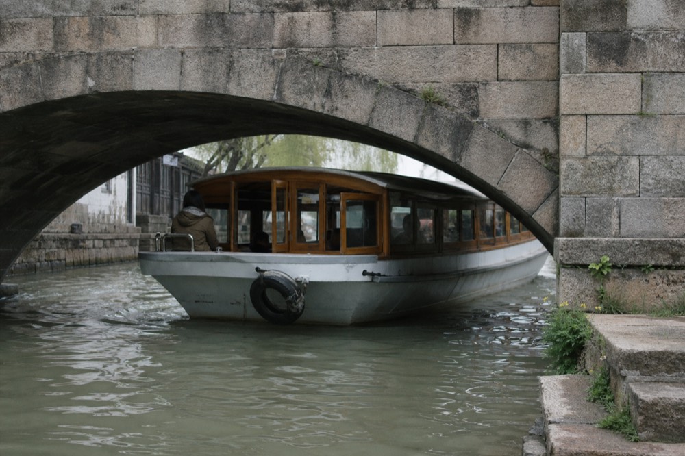 A canal cruise boat passing under a stone bridge in central Amsterdam, no text, no logos, no people