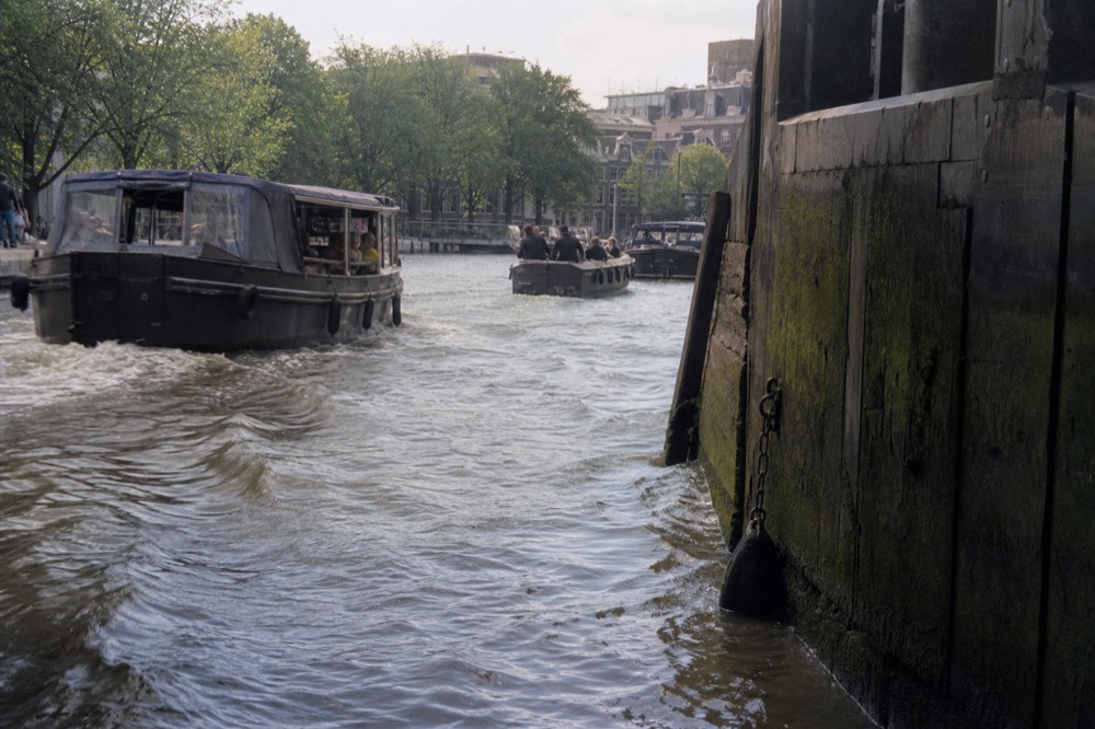 Canal boats passing in a busy Amsterdam waterway near the city centre, no text, no logos, no people