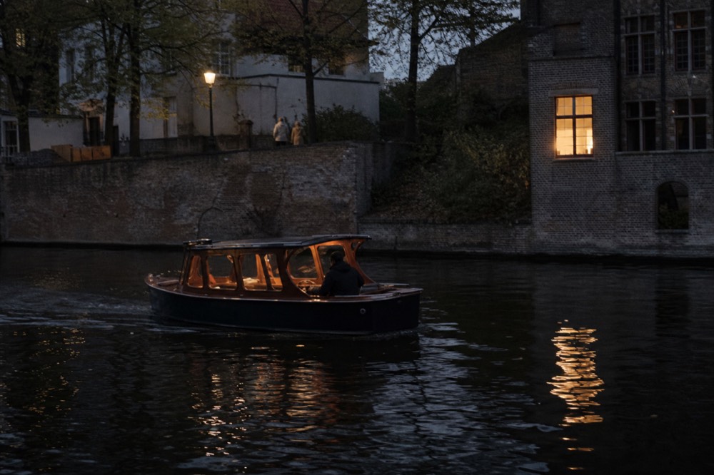 Small classic saloon boat gliding along an Amsterdam canal at dusk, no text, no logos, no people