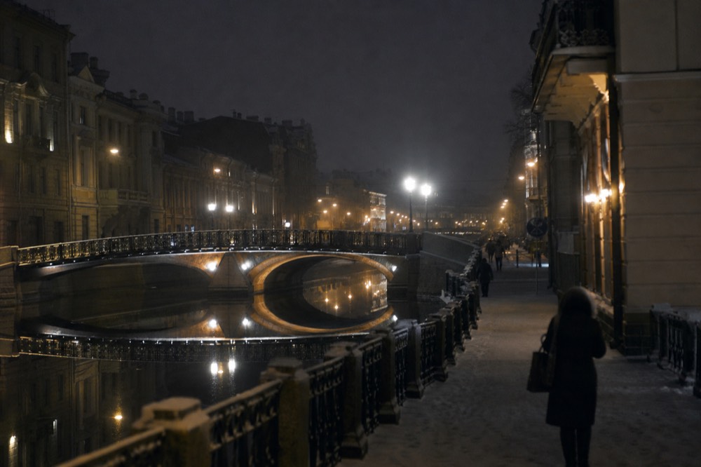 Illuminated Amsterdam canal at night with lit bridges reflecting in dark water, no text, no logos, no people