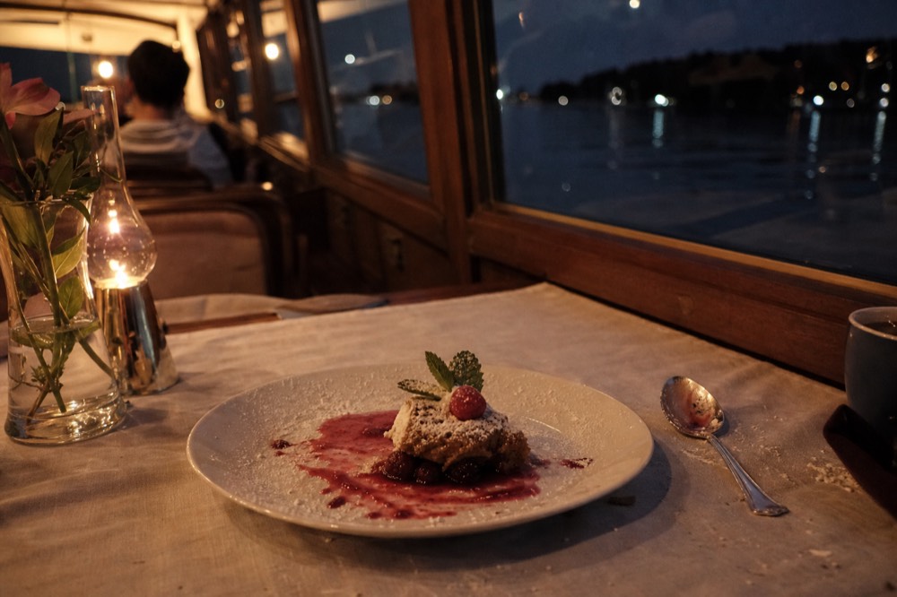 An elegant plated dessert course on a linen-covered table aboard a small canal cruise boat, no text, no logos, no people.
