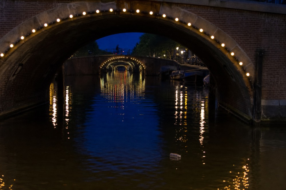 Amsterdam canal bridges lit at night reflecting in dark water, no text, no logos, no people