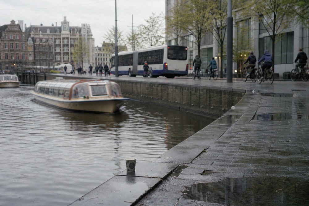 A canal cruise boat passing a busy Amsterdam quay with a bus in the background, no text, no logos, no people