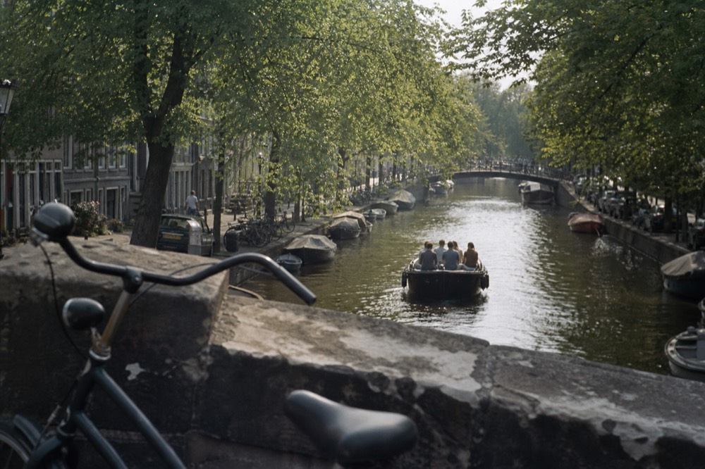 A canal cruise boat seen from a bridge with the Amsterdam canal ring stretching behind it, no text, no logos, no people
