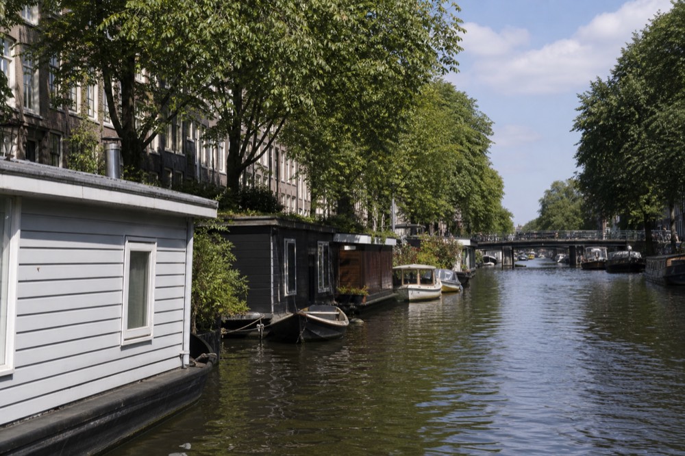 Quiet canal lined with trees and houseboats, no text, no logos, no people
