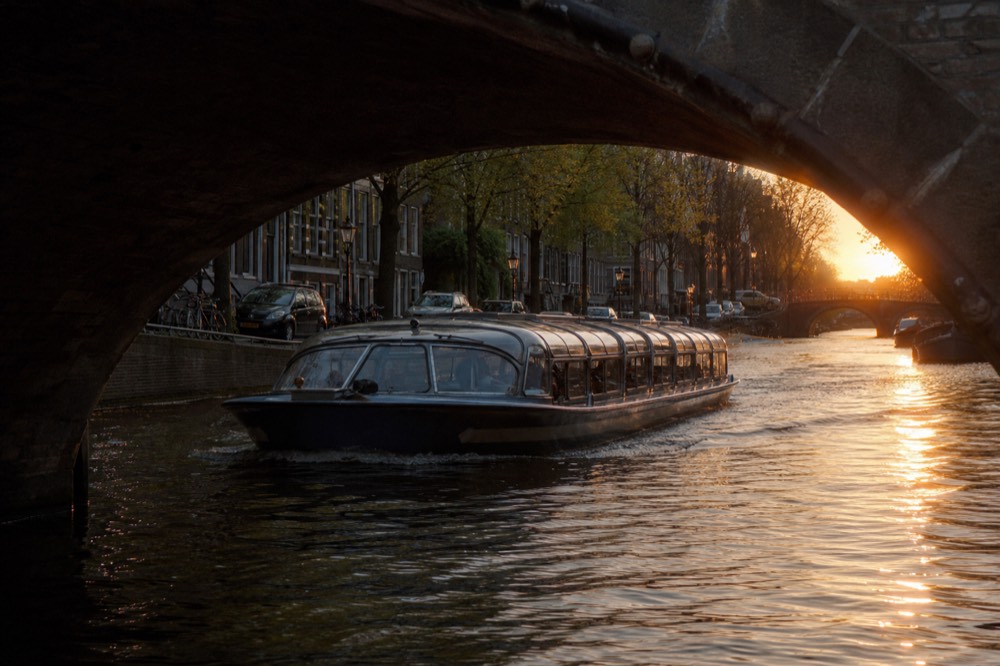 Classic canal cruise boat passing under a low stone bridge, no text, no logos, no people