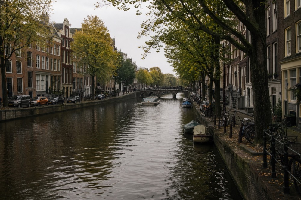 Historic Amsterdam canal with a tour boat in the distance, no text, no logos, no people