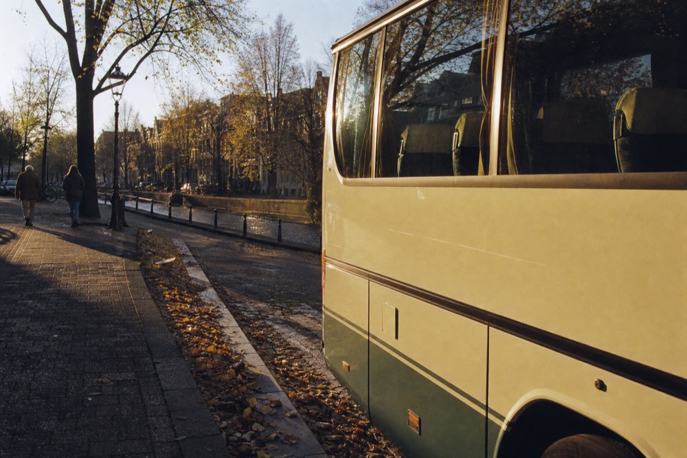 A sightseeing bus parked on an Amsterdam street beside a canal, no text, no logos, no people
